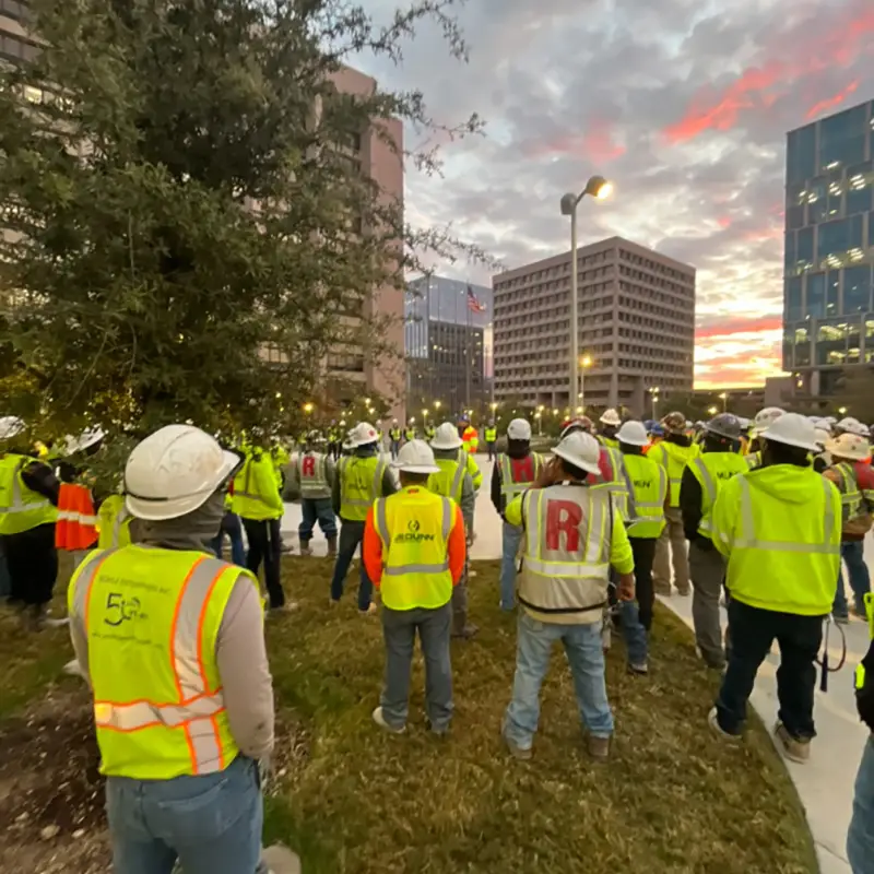 Trade workers gather for a safety toolbox talk in the early morning hours on the Phase II construction site.
